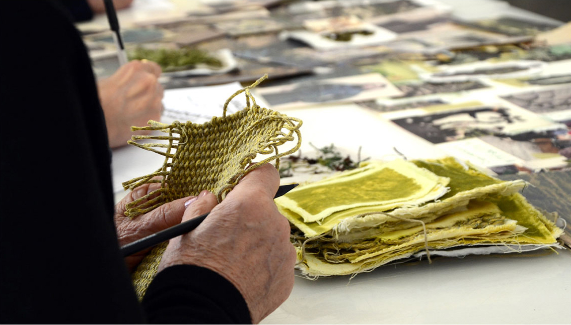 Mano che analizza campioni di tessuti su tavolo da lavoro, evidenziando texture, qualità e scelta dei materiali.