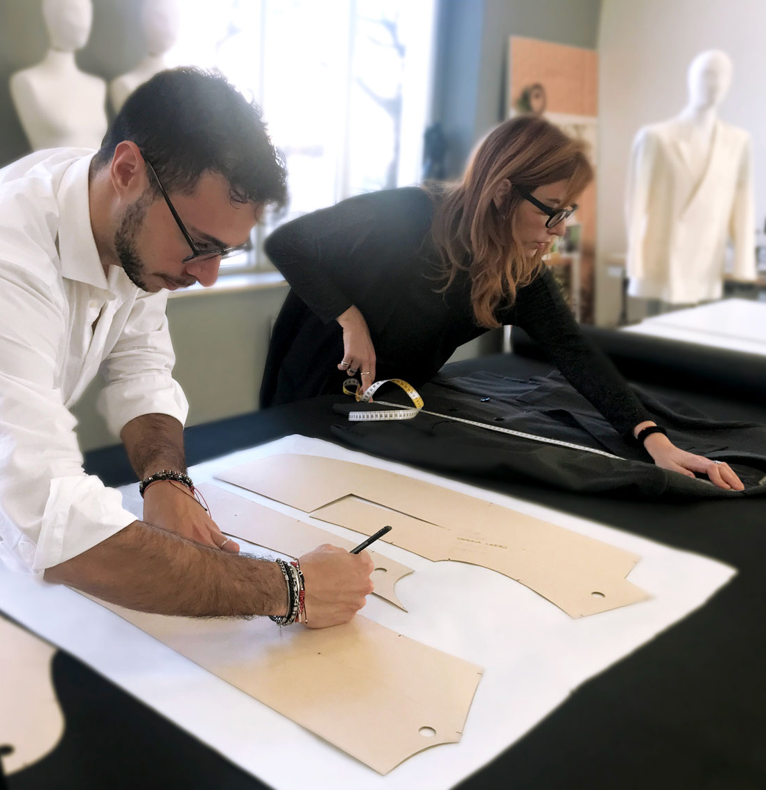 Docenti di modellistica mentre tracciano i contorni di un cartamodello su un grande tavolo da taglio in un laboratorio moda.