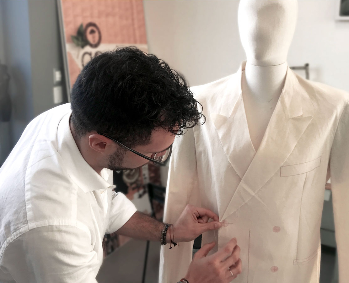 Modellista che lavora su un manichino sartoriale, appuntando e modellando il tessuto di una giacca per definirne la struttura.